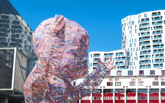 Sculpture of a transparent baby in Rotterdam with modern buildings in the background.