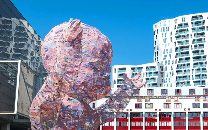 Sculpture of a transparent baby in Rotterdam with modern buildings in the background.