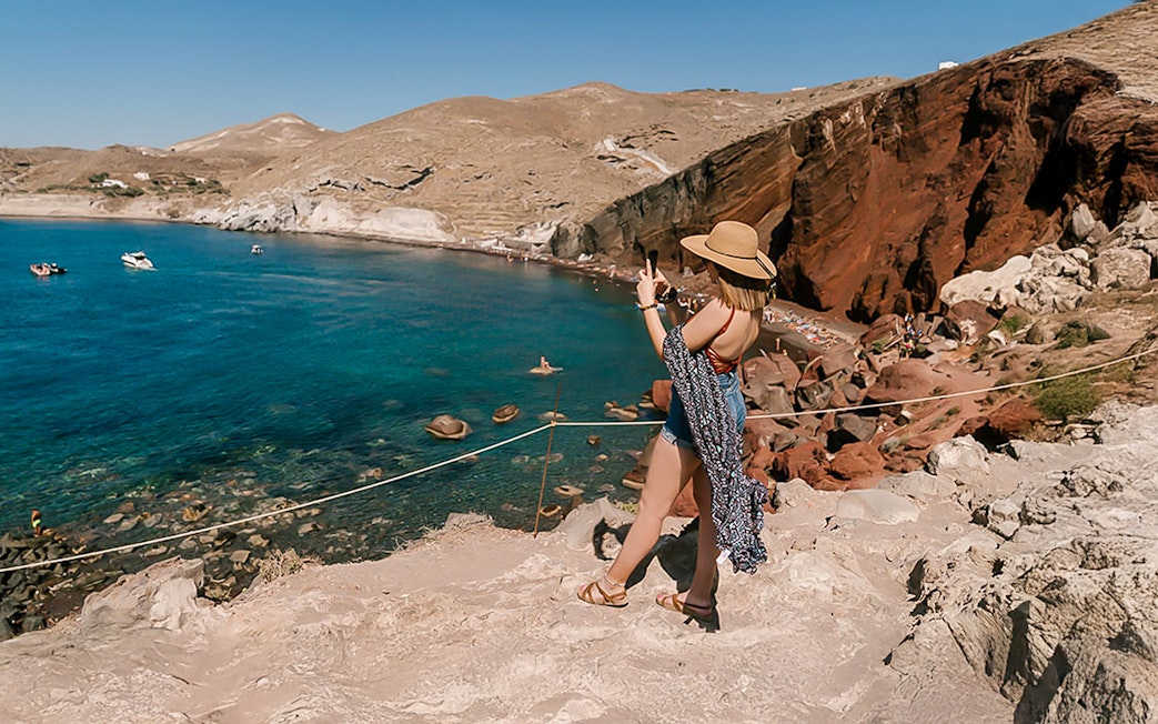 Guests taking photos at Red Beach, Santorini, with clear blue waters and red cliffs.