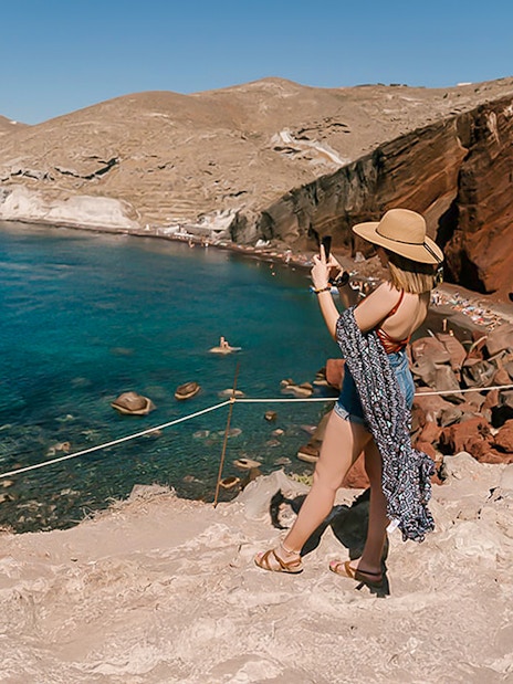 Guests taking photos at Red Beach, Santorini, with clear blue waters and red cliffs.