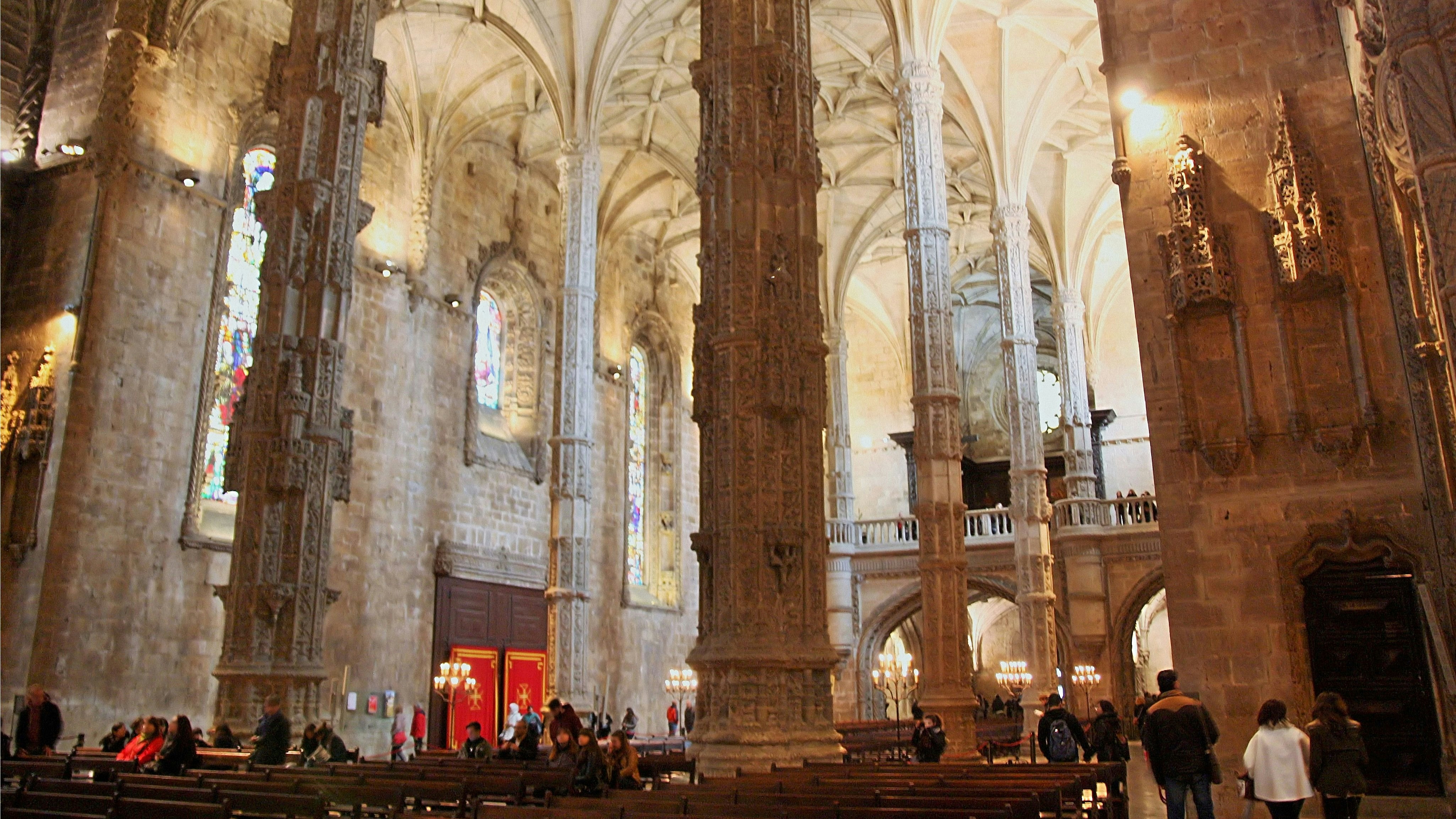 Nave of the Church of Santa Maria de Belem in Jeronimos Monastery with ornate columns and stained glass windows.