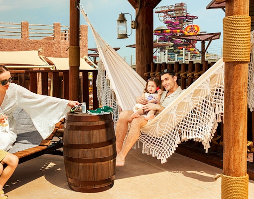 Family relaxing in a hammock at Meryal Waterpark with colorful slides in the background.