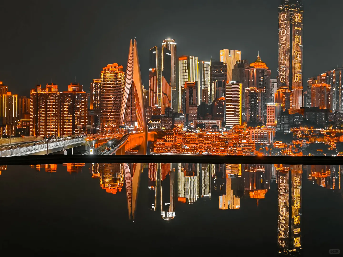 Chongqing skyline at night with illuminated skyscrapers and bridge reflecting in water.