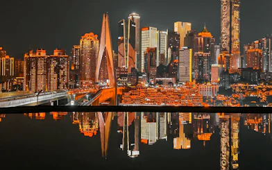 Chongqing skyline at night with illuminated skyscrapers and bridge reflecting in water.