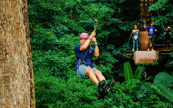 Tourist zip lining through lush forest at Hanuman World Zipline, Thailand.