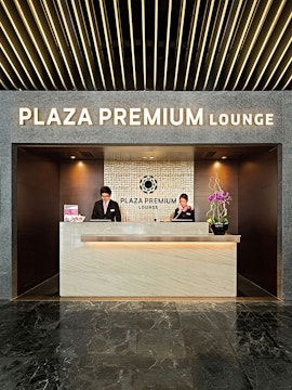 Reception desk at Plaza Premium Lounge in Macau with staff members assisting guests.