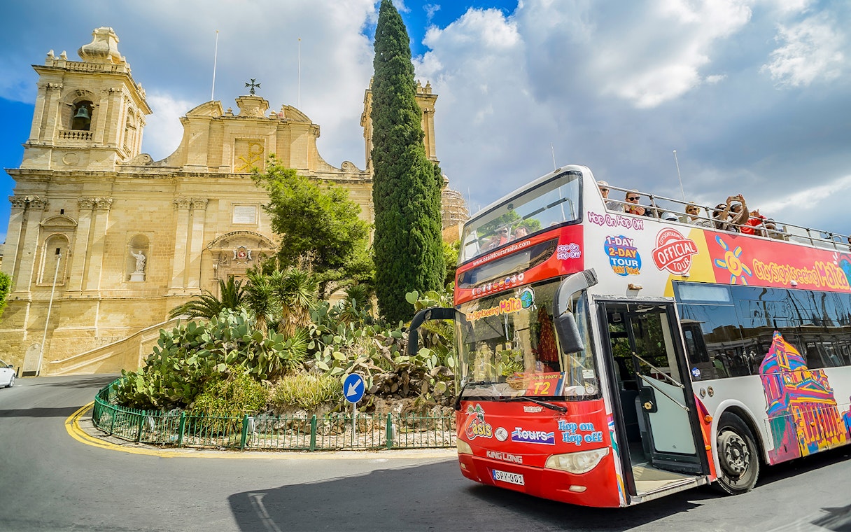 Hop-on-hop-off tour bus in front of a historic building in Malta.