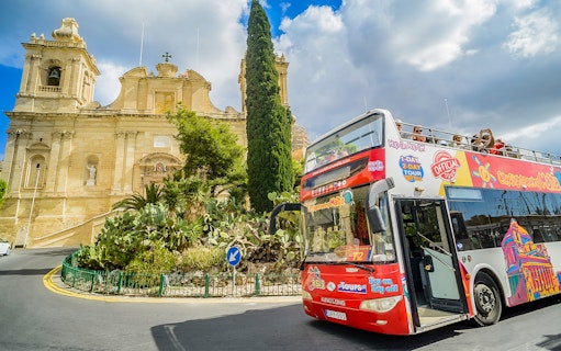 Hop-on-hop-off tour bus in front of a historic building in Malta.