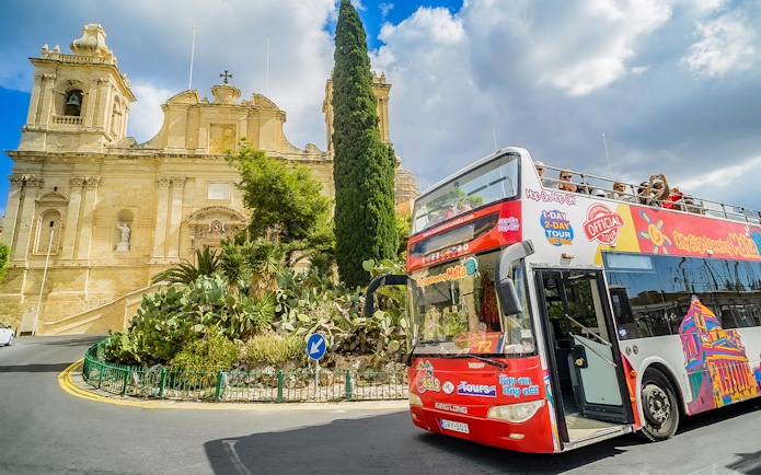 Hop-on-hop-off tour bus in front of a historic building in Malta.