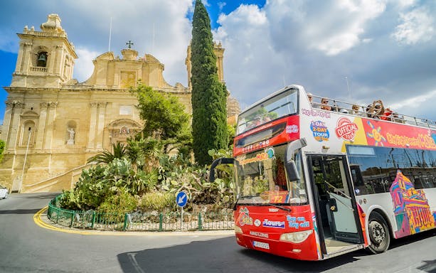 Hop-on-hop-off tour bus in front of a historic building in Malta.