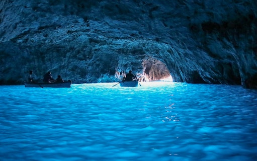 Boat entering Blue Grotto cave with glowing blue water, Capri tour from Rome.