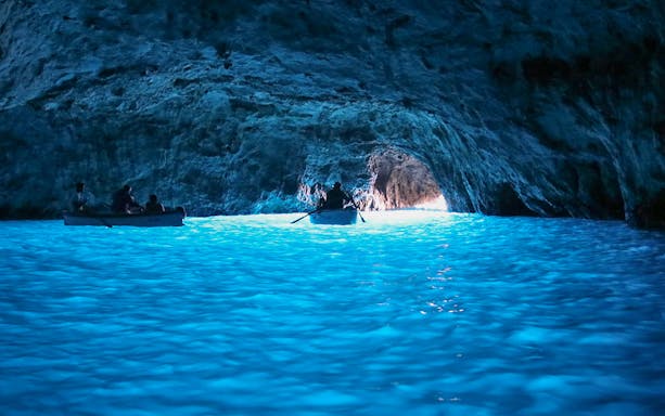Boat entering Blue Grotto cave with glowing blue water, Capri tour from Rome.