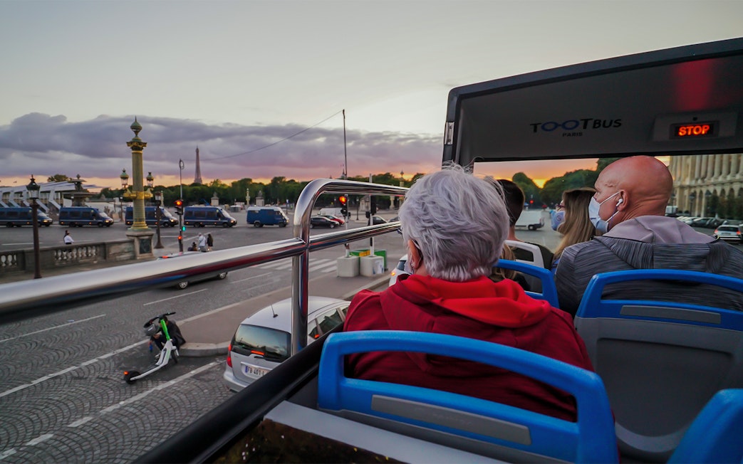 Open-top bus tour in Paris with view of Eiffel Tower at sunset.