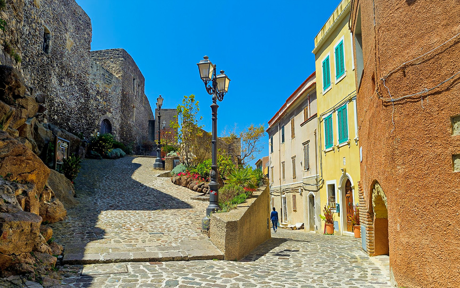 Cobblestone street in Castelsardo with historic buildings and street lamps.
