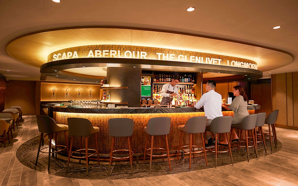 Bar area in first-class lounge at Hong Kong International Airport with bartender serving guests.