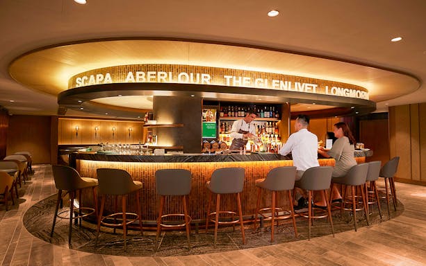 Bar area in first-class lounge at Hong Kong International Airport with bartender serving guests.