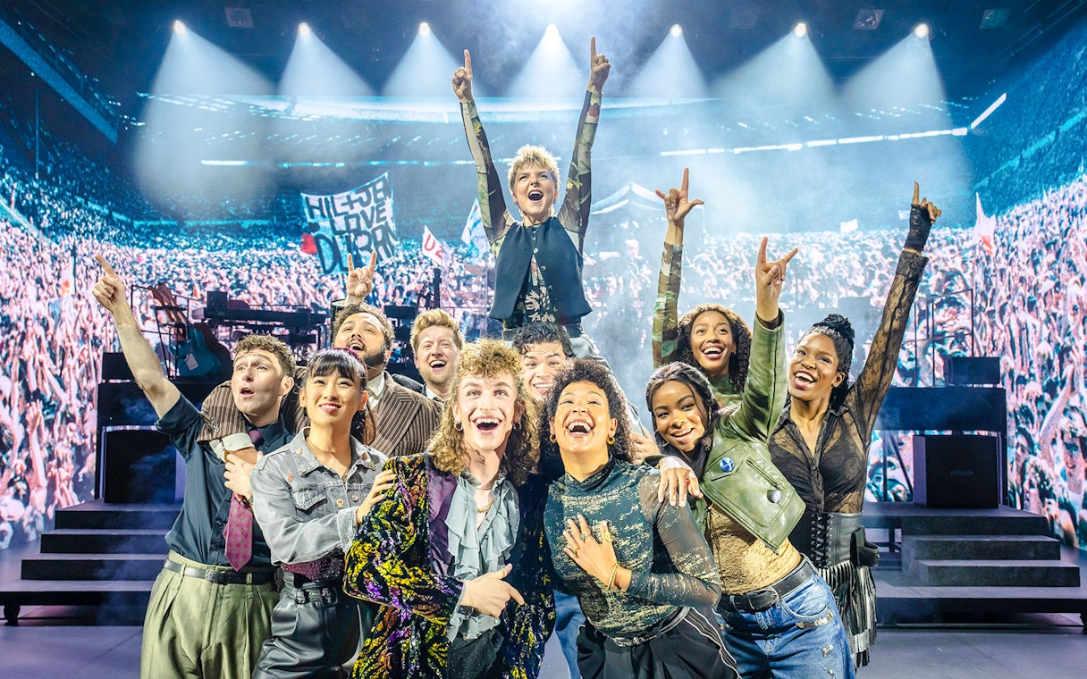 Performers on stage at Just for One Day concert with cheering crowd.