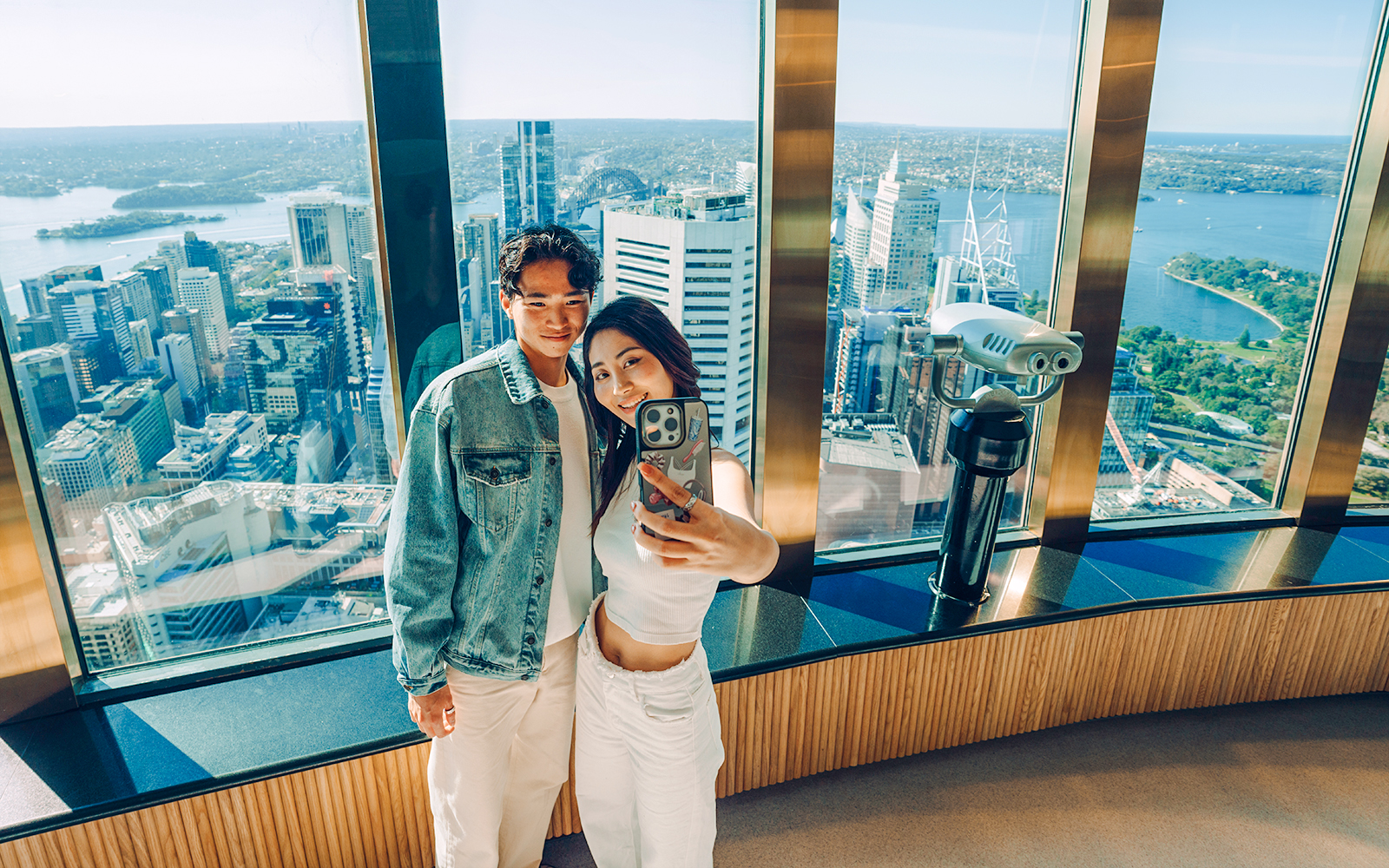 Couple taking a selfie on the viewing deck of Sydney Tower Eye with cityscape.