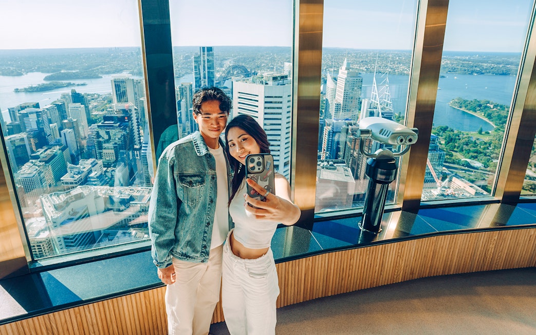 Couple taking a selfie on the viewing deck of Sydney Tower Eye with cityscape.