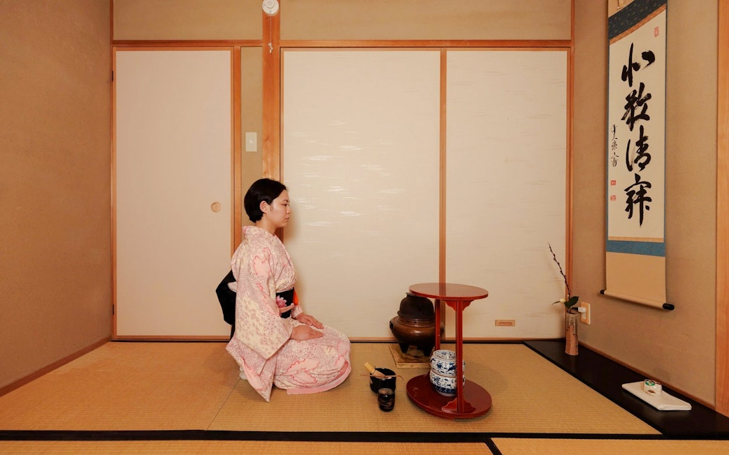 Person in kimono performing traditional tea ceremony in Japanese tatami room.