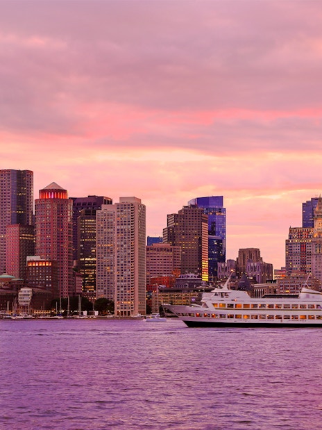 Boston skyline at sunset with boats on the water.