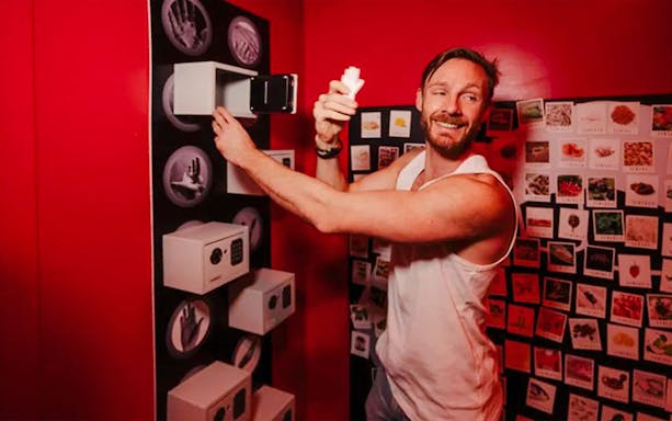 Man participating in a SENSAS challenge, interacting with a wall of safes in a red room.