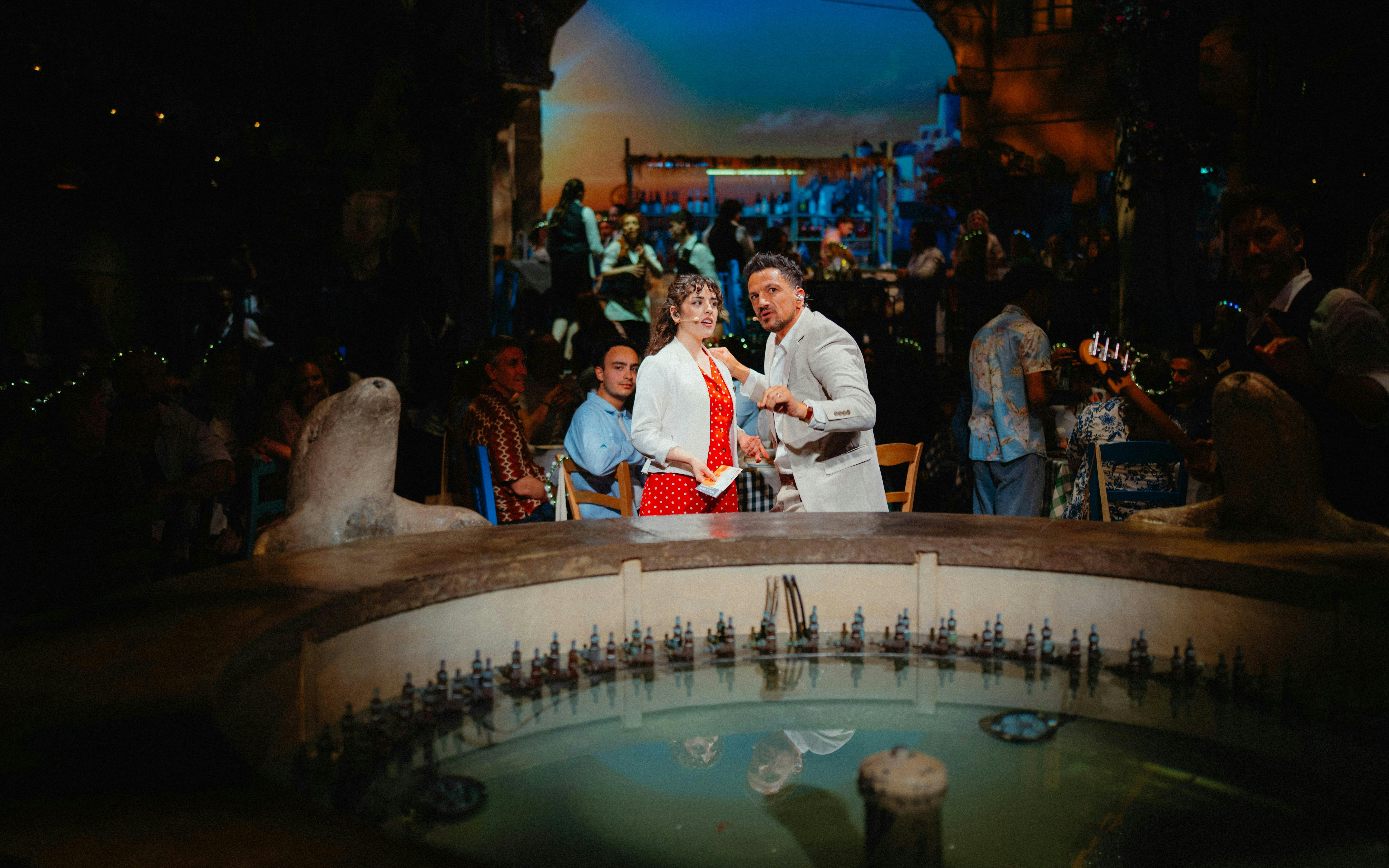 Guests enjoying Mamma Mia! The Party performance with actors near a fountain.