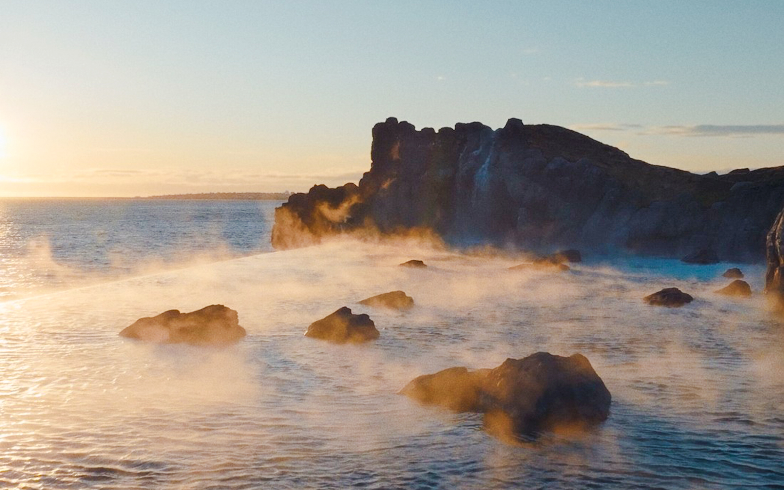 Infinity pool at Sky Lagoon with ocean view and rocky shoreline at sunset.