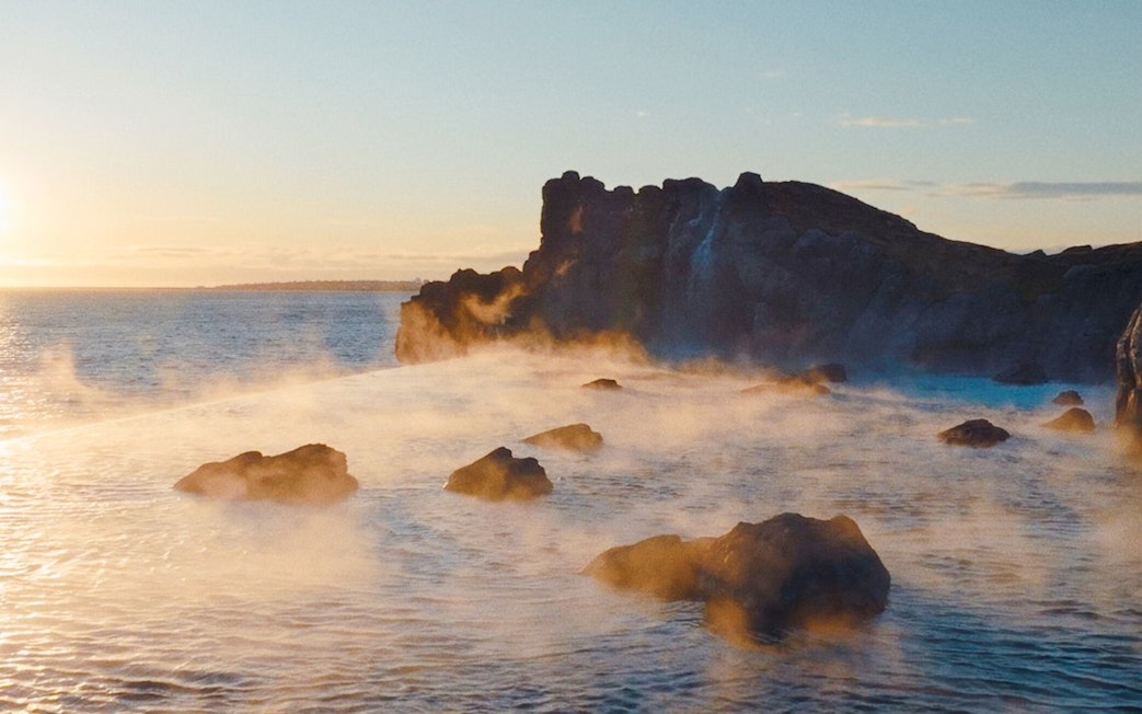 Infinity pool at Sky Lagoon with ocean view and rocky shoreline at sunset.