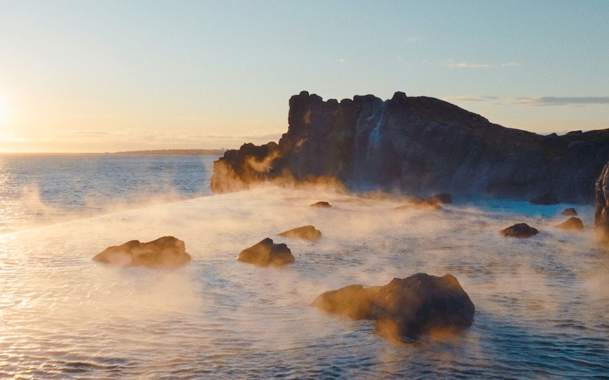 Infinity pool at Sky Lagoon with ocean view and rocky shoreline at sunset.