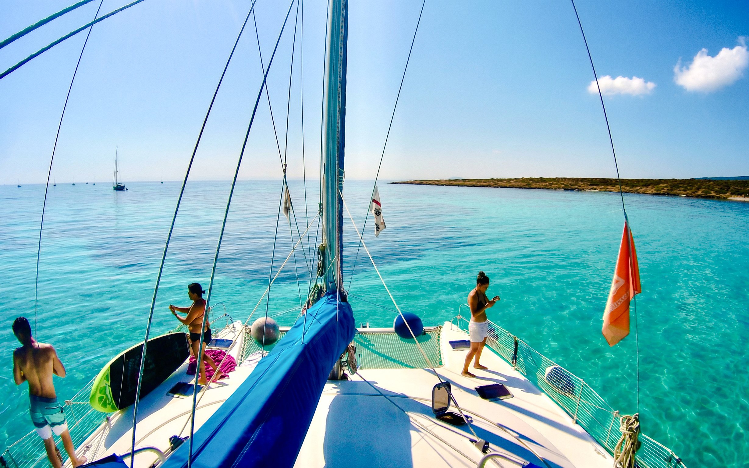 Catamaran sailing in La Maddalena Archipelago with clear blue waters and distant coastline.