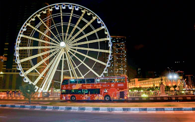 Red double-decker bus in front of illuminated Ferris wheel on Sharjah Hop-On-Hop-Off Bus Tour.