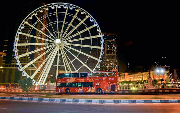Red double-decker bus in front of illuminated Ferris wheel on Sharjah Hop-On-Hop-Off Bus Tour.