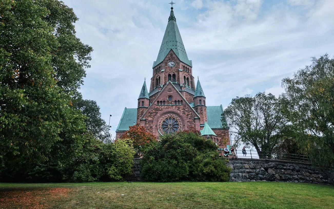 Stockholm church with green spires surrounded by trees, part of a self-guided city exploration game.