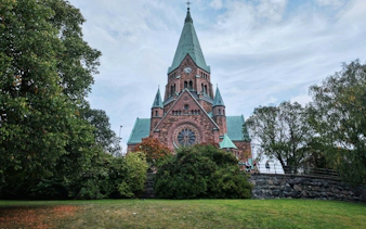 Stockholm church with green spires surrounded by trees, part of a self-guided city exploration game.