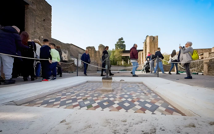 Tourists exploring the ancient ruins of Pompeii, Italy, near a mosaic floor.