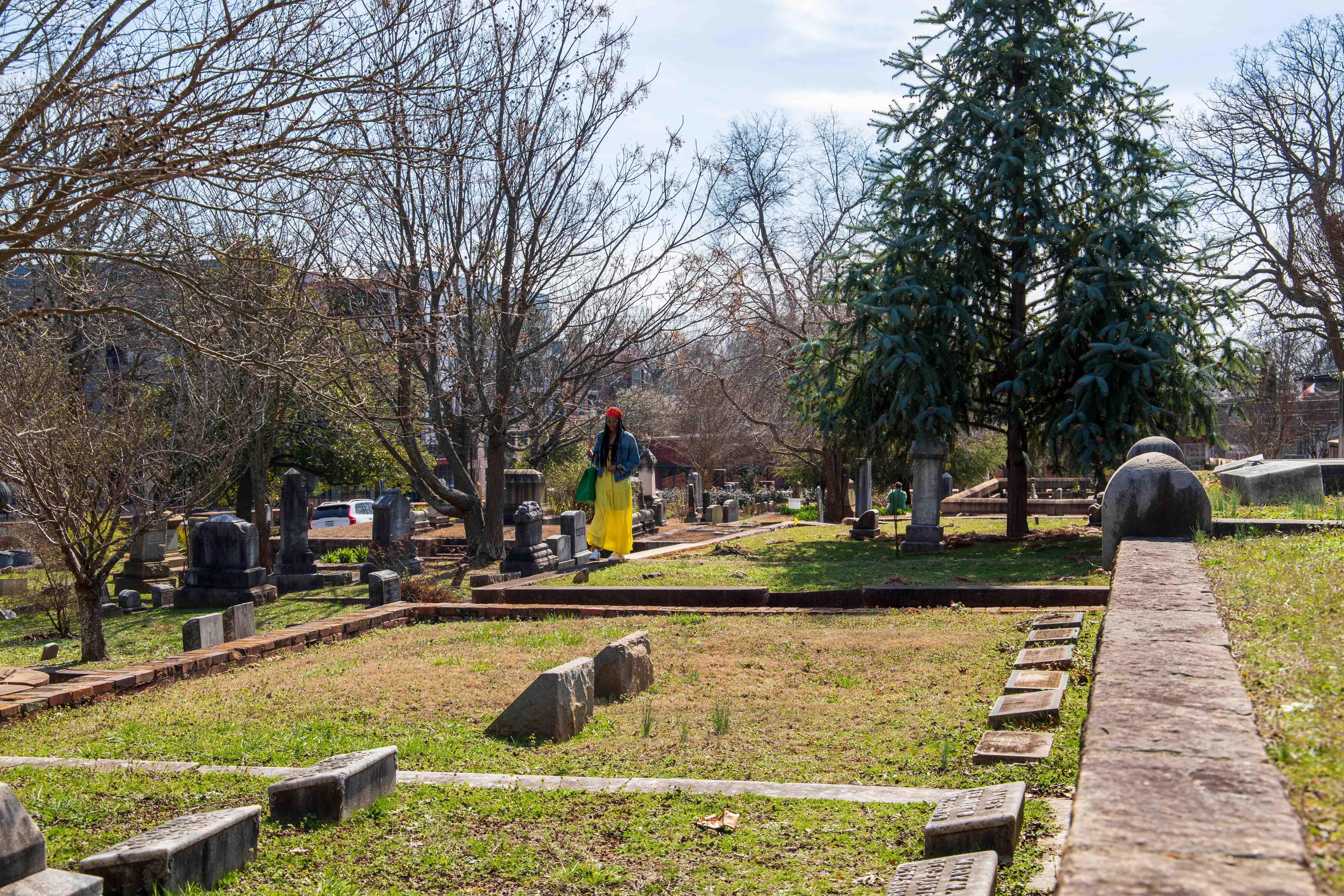 Person walking through Green-Wood Cemetery with gravestones and trees in view.