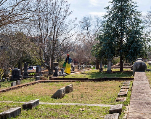 Person walking through Green-Wood Cemetery with gravestones and trees in view.