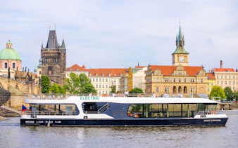 Electric boat cruising on the Vltava River with Prague's historic buildings in the background.