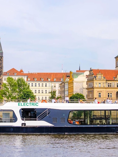 Electric boat cruising on the Vltava River with Prague's historic buildings in the background.