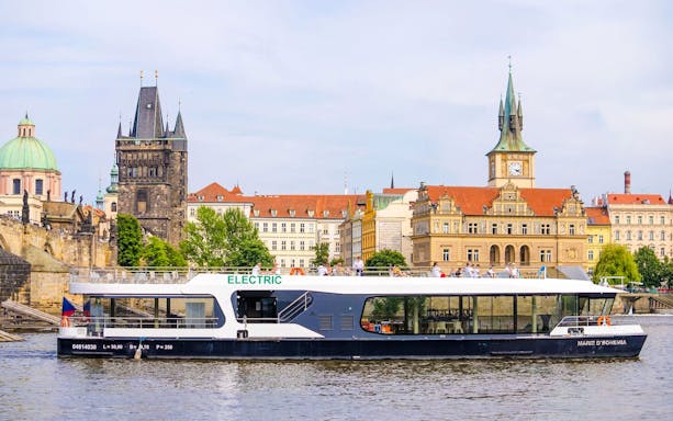 Electric boat cruising on the Vltava River with Prague's historic buildings in the background.