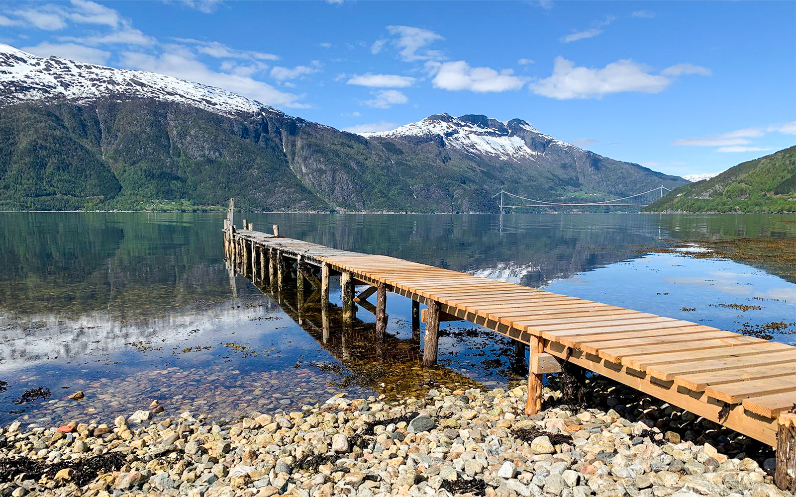 Walkway leading to Hardangerfjorden lake with snow-capped mountains in Norway.