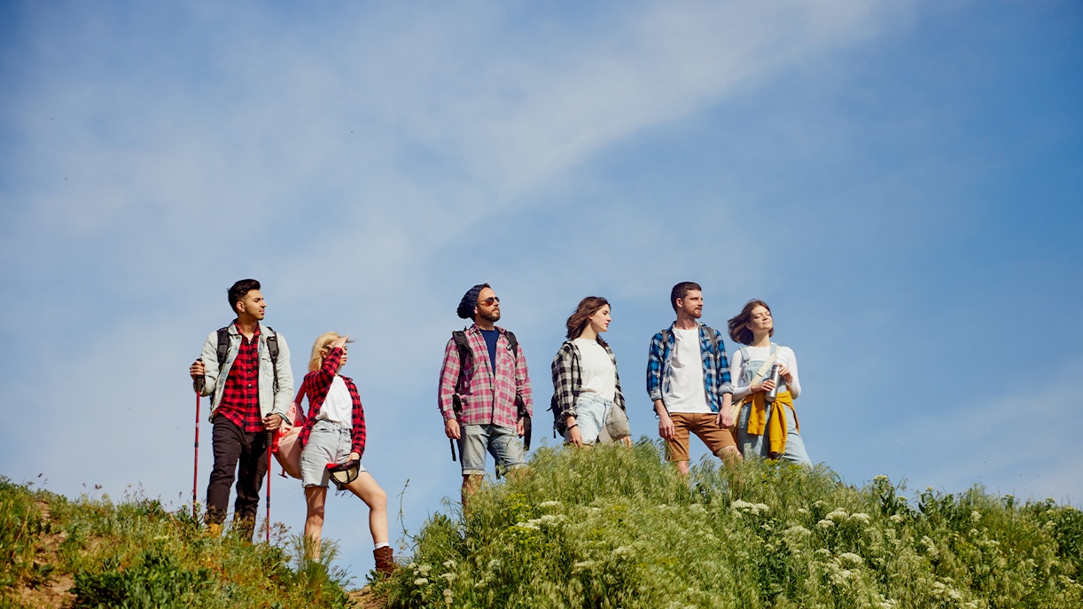 Friends trekking through a lush meadow with scenic mountain views in the background.