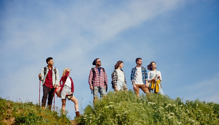 Friends trekking through a lush meadow with scenic mountain views in the background.