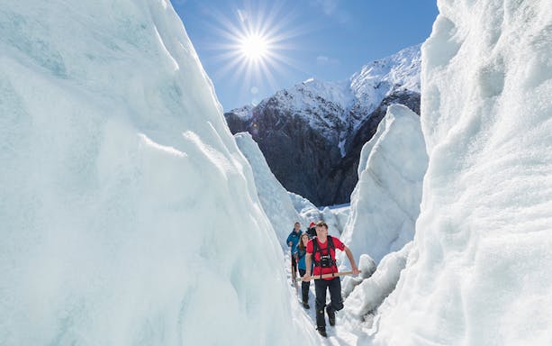 Hikers with guide navigating icy glacier path under bright sun.