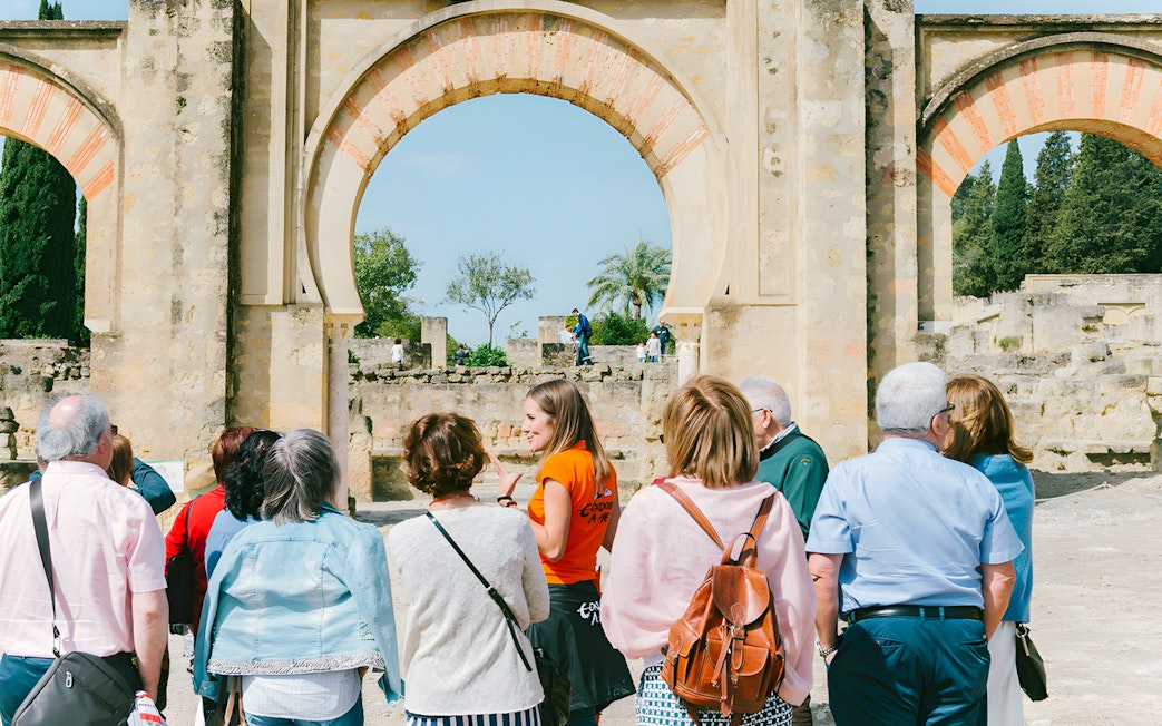 Guided group tour at Medina Azahara, Córdoba, with historical arches in the background.