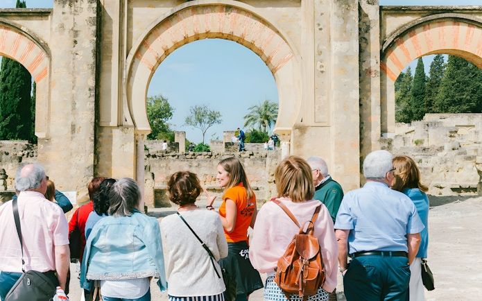 Guided group tour at Medina Azahara, Córdoba, with historical arches in the background.