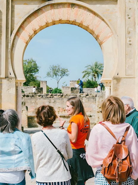 Guided group tour at Medina Azahara, Córdoba, with historical arches in the background.