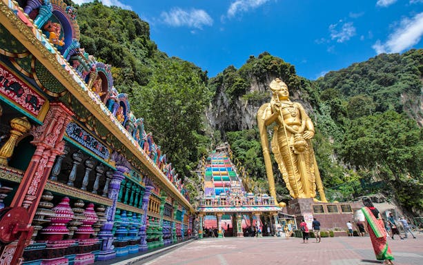 Batu Caves entrance with colorful steps and large golden statue in Kuala Lumpur.