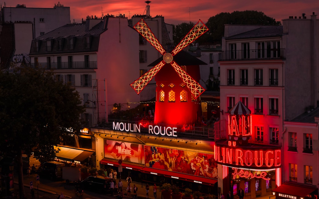 Moulin Rouge illuminated at sunset in Paris, featuring iconic red windmill.